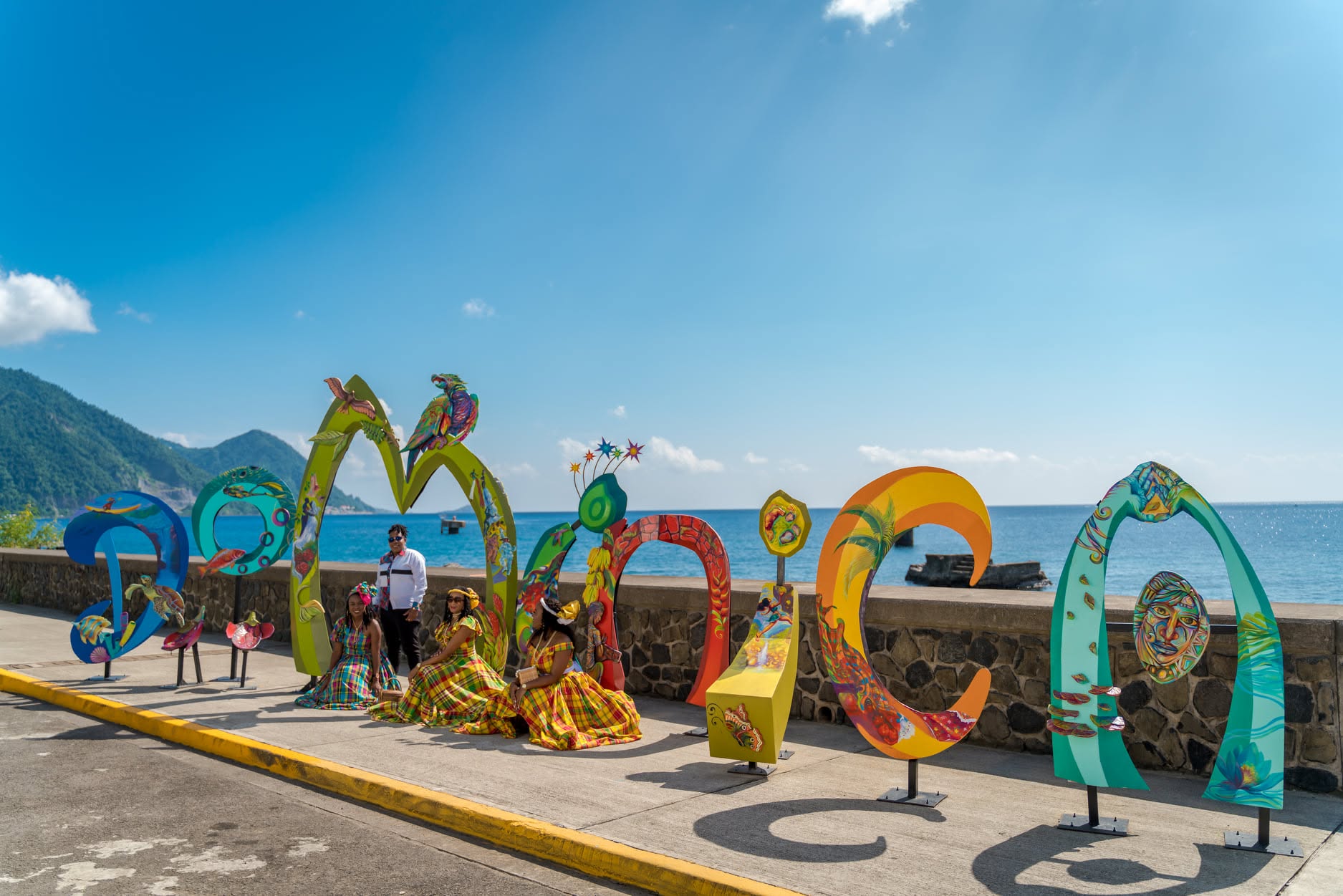 Visitors in traditional madras dress by the Dominica sign on the Roseau waterfront